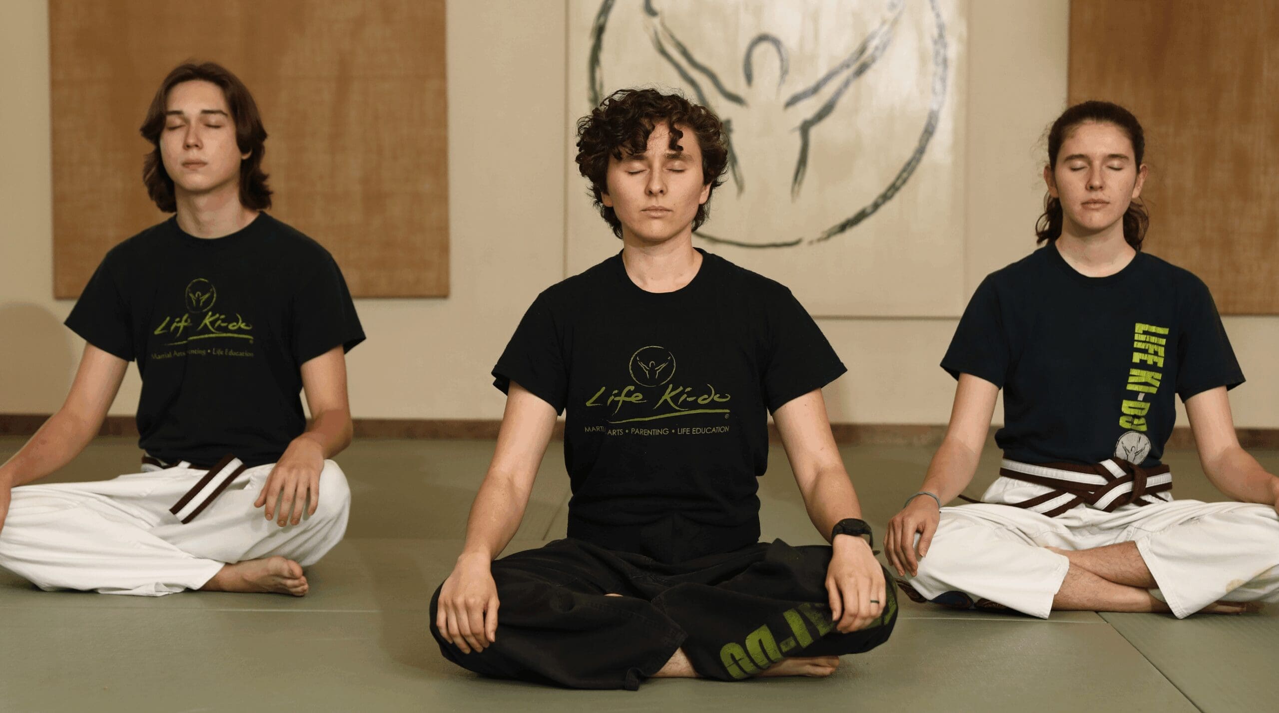 Three Life Ki-do students seated in a meditative posture on the dojo mat, representing breath awareness, inner calm, and personal development through martial arts