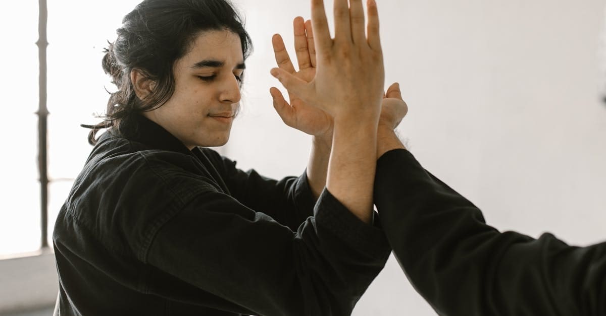 Close-up of a student in a black uniform focusing on hand-to-hand blocking drills with their instructor during a self defense training for beginners class.