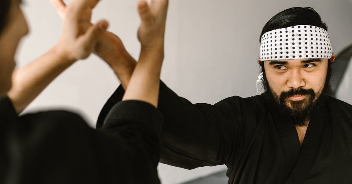 Close-up of a martial arts instructor wearing a patterned headband directing a student during self defense training for beginners, demonstrating hand blocking and deflection techniques.