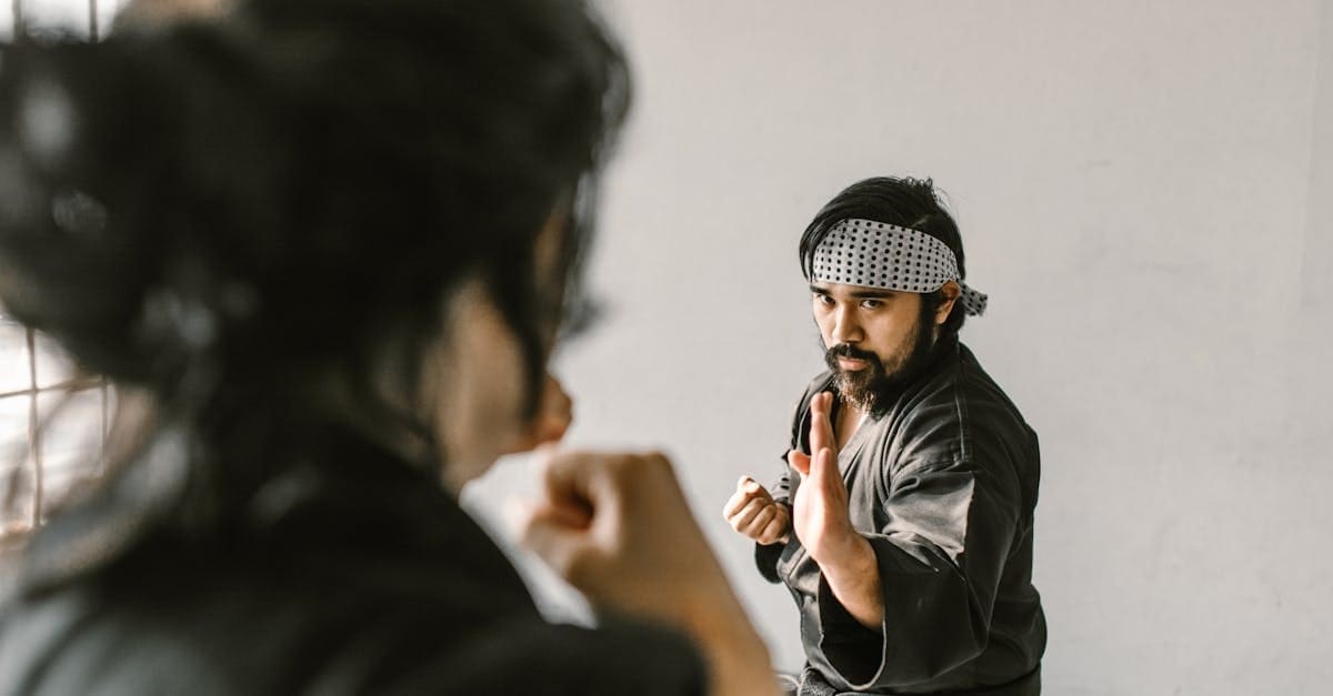 Over-the-shoulder view of a martial arts instructor in a black uniform demonstrating a defensive open-hand guard stance during a self defense training for beginners session.