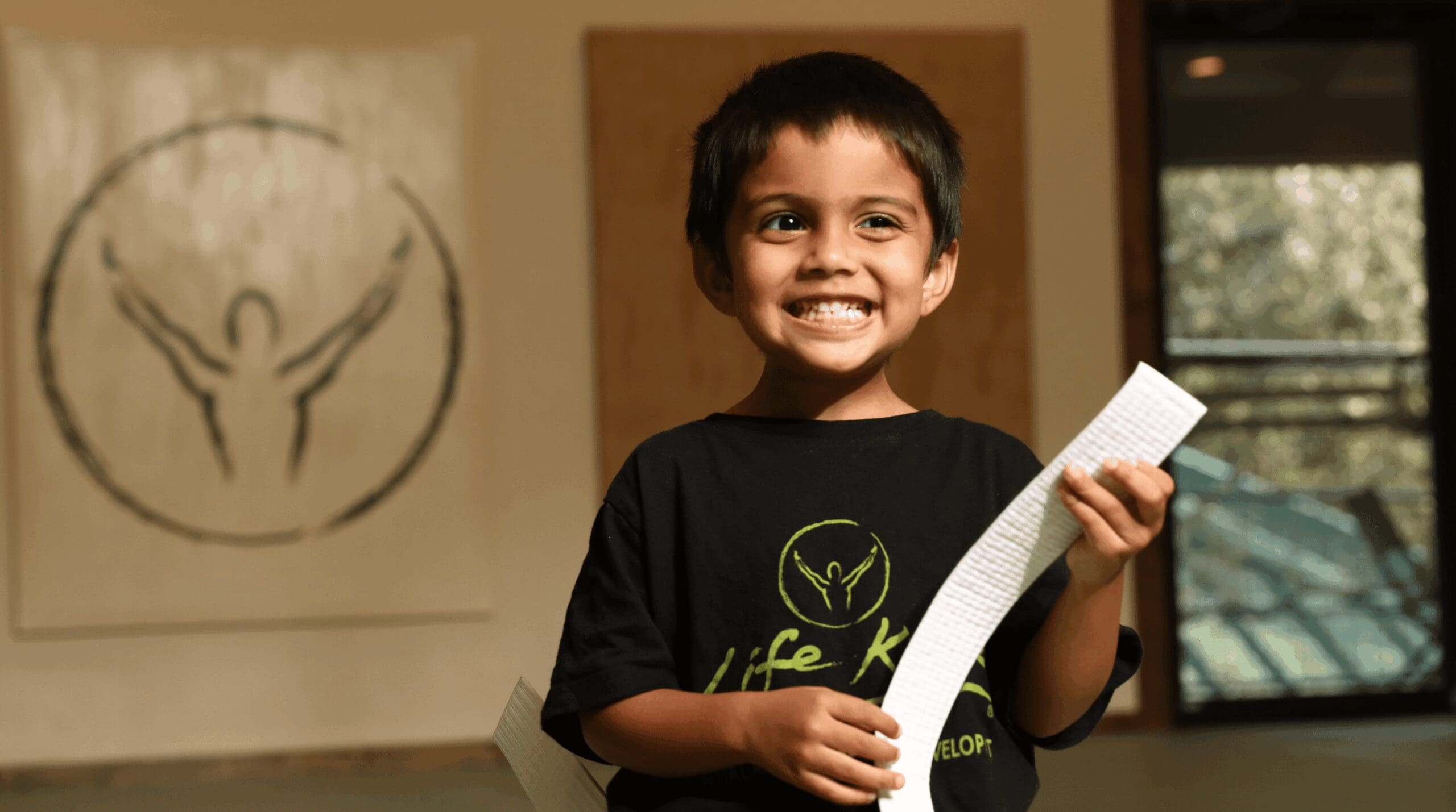 Smiling preschool martial arts student proudly holding a new white belt after class, celebrating confidence and achievement.