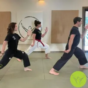 Three students practicing a wide Tai Chi stance with coordinated arm positions during an indoor class focused on tai chi breathing techniques.