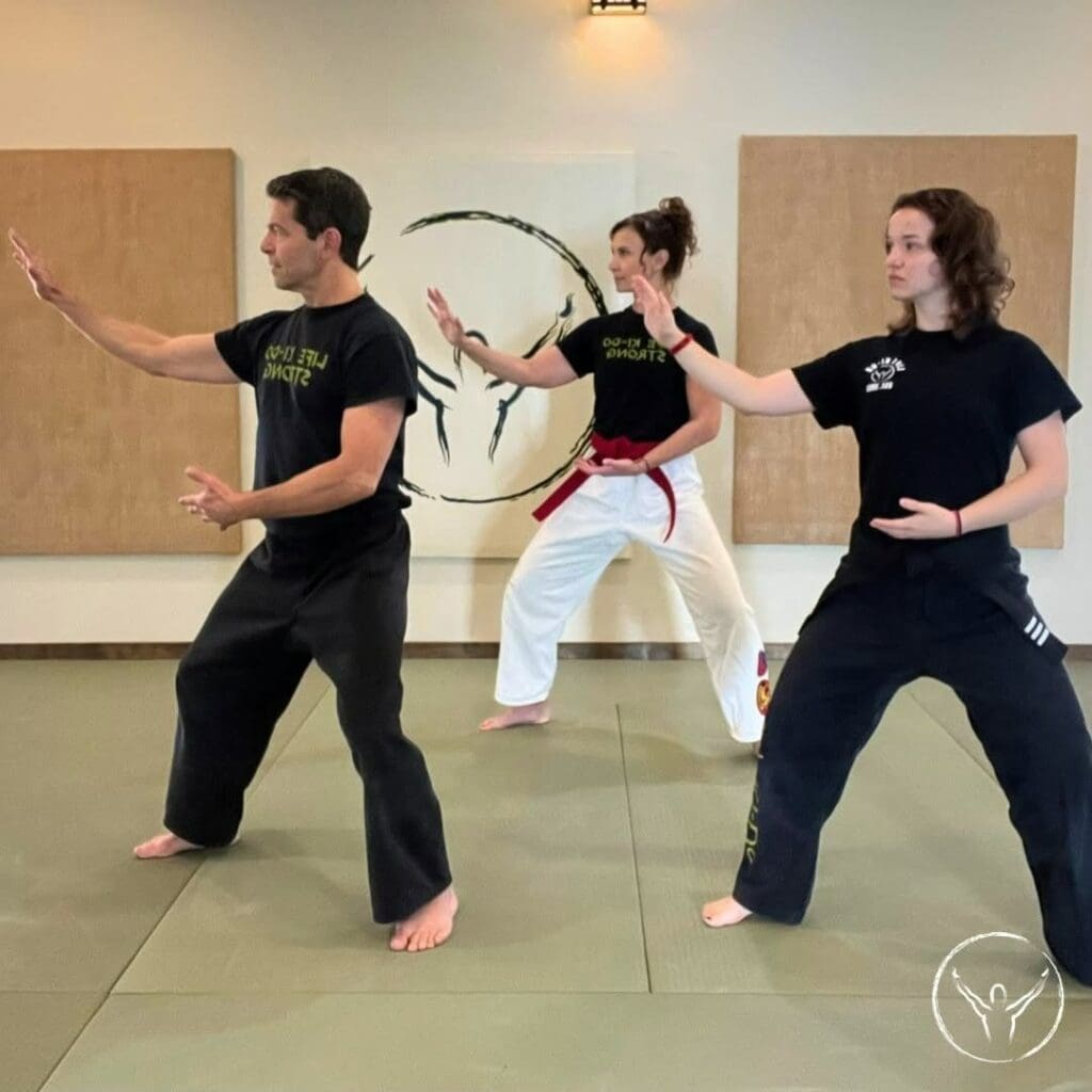 An instructor and two students moving through a controlled Tai Chi form during a studio lesson on tai chi breathing techniques.