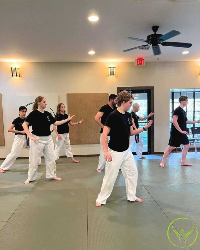 A group of students practicing slow, balanced Tai Chi movements in a martial arts studio while learning tai chi breathing techniques.